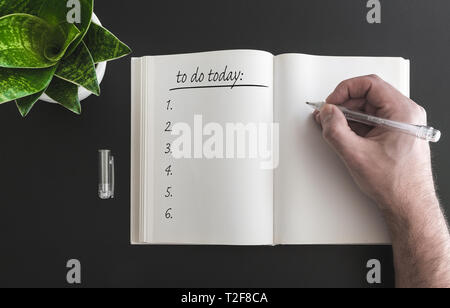 close-up of hand holding pen writing to do list in open book on desk Stock Photo
