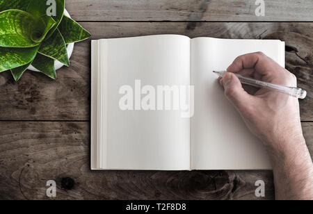 close-up top view of man writing in blank book with pen on wooden desk Stock Photo