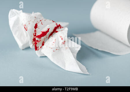 A photo of used bloody toilet paper and a toilet paper roll on the light blue background. Menstrual or hemorrhoids bleeding