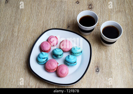 Two cups of coffee and a plate with blue and pink macarons with blueberry and raspberry filling Stock Photo