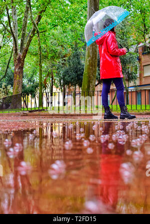 A young girl walks alone on a rainy day through a park under an umbrella Stock Photo