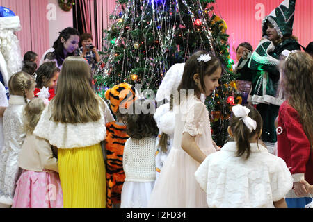 a lot of beautiful elegant children girls in dresses and boys in fancy dress having fun at the new year party around the Christmas tree Stock Photo