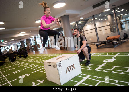 02 April 2019, North Rhine-Westphalia, Köln: Personal trainer Matthias shows Model Desiree an exercise on a jumping box during a press meeting at the fitness fair FIBO. FIBO sees itself as the world's largest trade fair for fitness, wellness and health. From 4 to 7 April 2019, more than 1,100 exhibitors from Europe and other regions of the world will be presenting their innovations in Cologne. Photo: Marius Becker/dpa Stock Photo