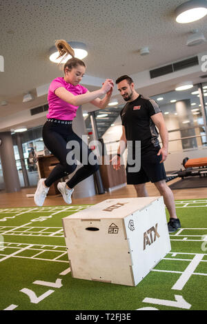 02 April 2019, North Rhine-Westphalia, Köln: Personal trainer Matthias shows Model Desiree an exercise on a jumping box during a press meeting at the fitness fair FIBO. FIBO sees itself as the world's largest trade fair for fitness, wellness and health. From 4 to 7 April 2019, more than 1,100 exhibitors from Europe and other regions of the world will be presenting their innovations in Cologne. Photo: Marius Becker/dpa Stock Photo