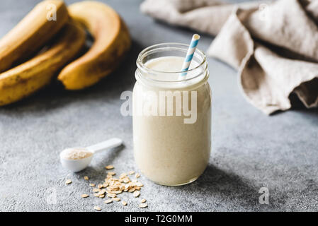 Protein banana smoothie in jar, protein scoop, oats and linen textile on table. Healthy vegan or vegetarian drink for sporty people Stock Photo