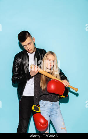 Sport games. Close up fashion portrait of two young cool hipster girl and boy wearing jeans wear. Woman with boxing gloves. Man with a baseball bat. S Stock Photo