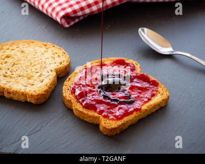 Pouring chocolate syrup on a slice of toast with raspberry jam Stock Photo