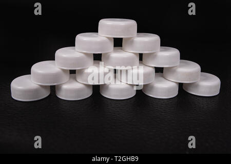 An organized group of used caps of plastic bottles on a black surface Stock Photo