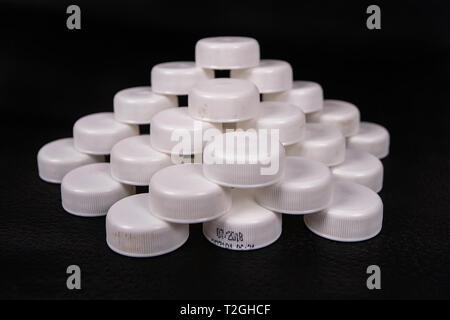 An organized group of used caps of plastic bottles on a black surface Stock Photo