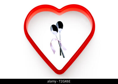 Two spoons tied together with pink ribbon.On a white background, surrounded by a red heart. Stock Photo