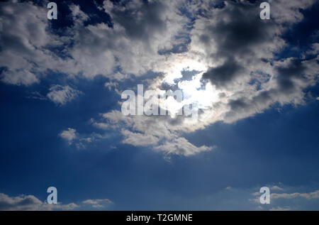bright sunshine behind clouds in blue sky background Stock Photo