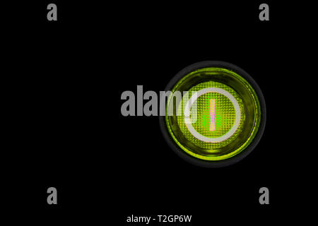Round green power (on and off) button or switch with retro illumination glowing in the dark macro photography and isolated on a dark black background. Stock Photo