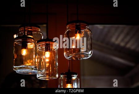 Retro vintage light bulbs inside empty DIY jar glasses as creative lamps hangings from the ceiling in house interior detail and blurred background. Stock Photo
