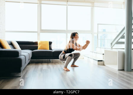 Fit young Pacific Islander woman training at home. Beautiful female athlete working out for wellbeing in domestic gym, training legs muscles with in a Stock Photo