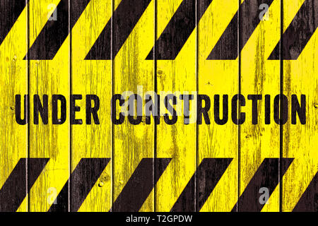 Under construction warning sign text with yellow black stripes painted on wood wall plank texture wide background. Concept do not enter the area, caut Stock Photo