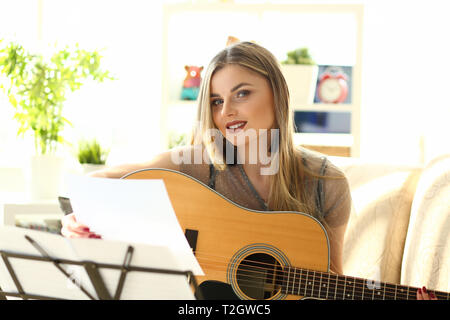 Millennial beautiful woman play guitar sit couch portrait. Misic scool concept home background. Stock Photo