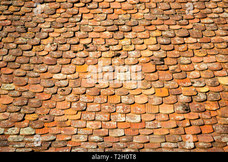 Abstract pattern of old, traditional, brown/orange, ceramic, overlapping shingles (tiles, schindle/schindel in German) on a house roof, lit in the mor Stock Photo
