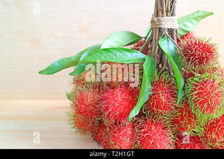 Bunch of Bright Color Red and Green Fresh Ripe Rambutan Fruits with Leaves Isolated on Wooden Table Stock Photo