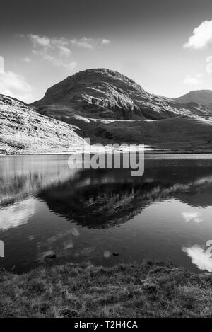 Black and White image of a  Fell in the Lake District is reflected in Styhead Tarn close to Scafell Pike. Stock Photo