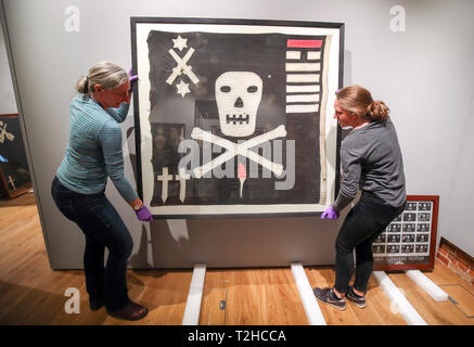 Exhibition staff at the National Museum of the Royal Navy, help hang a Jolly Roger from HMS Unison, during the preview of Jolly Roger: A Symbol of Terror and Pride exhibition at the National Museum of the Royal Navy at Portsmouth Historic Dockyard. Stock Photo