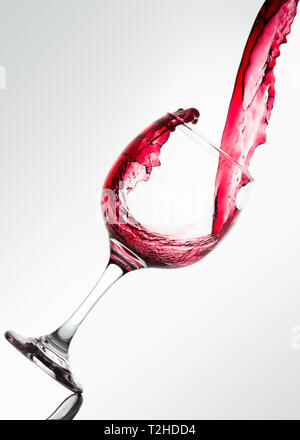 Wave formed on the pouring of red wine on a glass against a white background Stock Photo