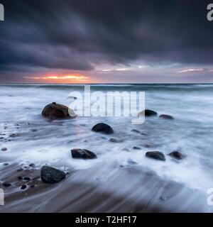 Stormy sea with dark clouds at sunset on the beach of the Baltic Sea, boulders in the surf, peninsula Fischland-Darss-Zingst, Western Pomerania Stock Photo