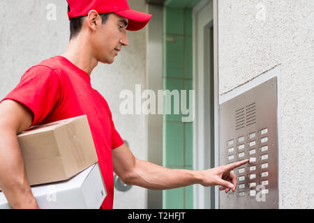 Delivery man with cardboard boxes pressing button of intercom to enter building Stock Photo