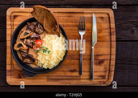 Top view frying pan with tasty beef stroganoff with mushrooms and couscous served in restaurant with fork and knife Stock Photo