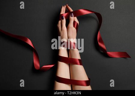 partial view of female hands in silk red ribbon on black background Stock Photo