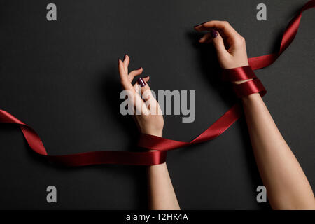 partial view of female hands in red ribbon on black background Stock Photo