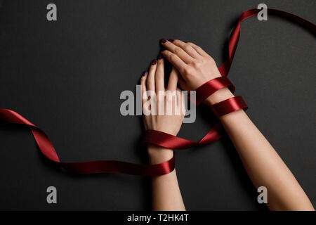 partial view of female hands in satin red ribbon on black background Stock Photo