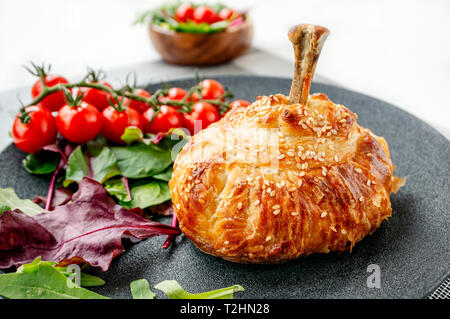 Chicken drumstick in dough baked in the oven with potatoes, tomatoes, onions and spices with a side dish of tomatoes and green salad. Stock Photo