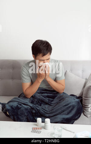 Man feeling cold, lying in the sofa and blowing his nose Stock Photo
