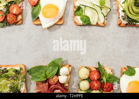Top view of toasts with vegetables, fried eggs and prosciutto on textured surface Stock Photo