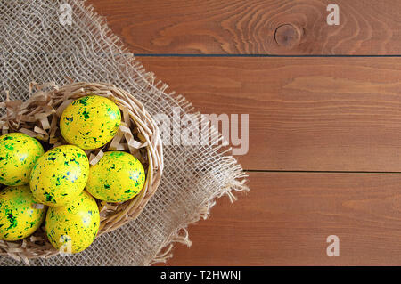 Easter eggs of yellow color with green splashes. On linen fabric brown. Wooden brown background. Stock Photo