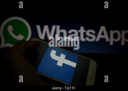 Facebook logo is shown on a smartphone display, WhatsApp logo unfocused on background Stock Photo