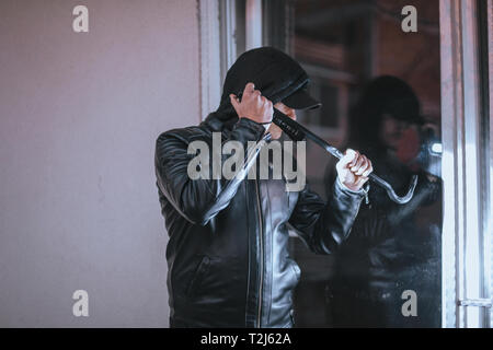 Housebreaker wearing black clothes and leather coat breaking in a house Stock Photo