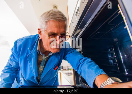 Repairman is standing in the kitchen and fixing the oven Stock Photo