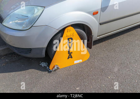 Untaxed vehicle immobilised at the roadside by a yellow DVLA clamp, for non-payment of road tax Stock Photo