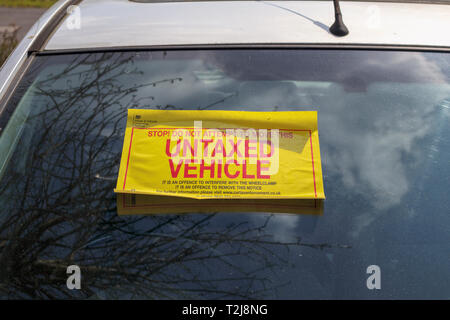 Untaxed vehicle sticker on the windscreen of a car immobilised at the roadside by a yellow DVLA clamp, for non-payment of road tax Stock Photo