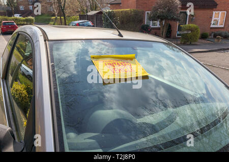 Untaxed vehicle sticker on the windscreen of a car immobilised at the roadside by a yellow DVLA clamp, for non-payment of road tax Stock Photo