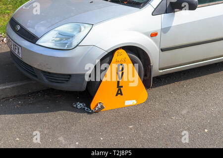 Untaxed vehicle immobilised at the roadside by a yellow DVLA clamp, for non-payment of road tax Stock Photo