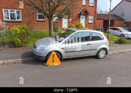 Untaxed car immobilised at the roadside by a yellow DVLA wheelclamp with sticker on the windscreen of non-payment of road tax Stock Photo