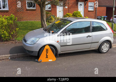 Untaxed car immobilised at the roadside by a yellow DVLA wheelclamp with sticker on the windscreen of non-payment of road tax Stock Photo