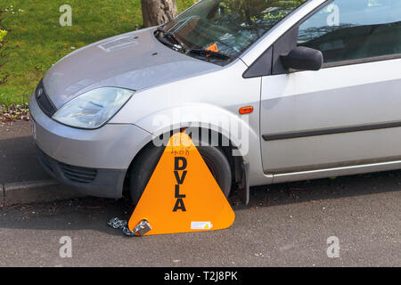 Untaxed vehicle immobilised at the roadside by a yellow DVLA clamp, for non-payment of road tax Stock Photo