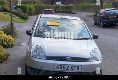 Untaxed vehicle sticker on the windscreen of a car immobilised at the roadside by a yellow DVLA clamp, for non-payment of road tax Stock Photo