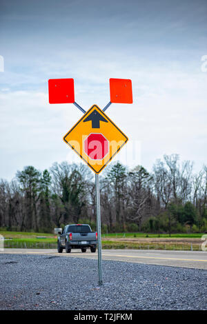 Vertical shot of a road sign warning of a new stop sign ahead beside a road with a truck on it under a blue cloudy sky. Stock Photo