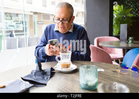 Handsome middle age senior man drinking coffee at restaurante, smiling happy enjoying and relaxing retirement using smartphone Stock Photo