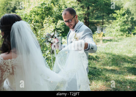 Bearded groom in a gray jacket and glasses holding a veil or wedding dress of the bride. Stock Photo