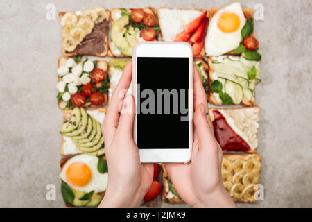 Cropped view of woman with toasts holding smartphone with blank screen Stock Photo
